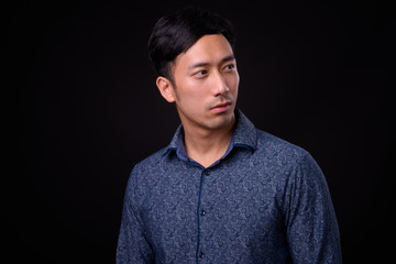 Young handsome Asian businessman against black background