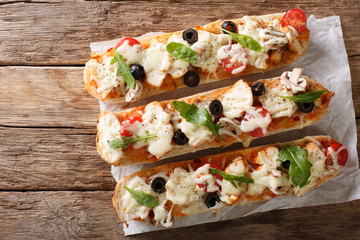 Hot tasty cut baguette baked with chicken, cheese, tomatoes, olives and mushrooms close-up....