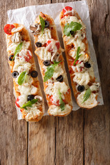 Hot tasty cut baguette baked with chicken, cheese, tomatoes, olives and mushrooms close-up....