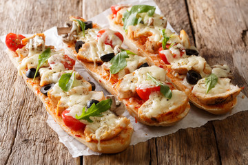 Hot tasty cut baguette baked with chicken, cheese, tomatoes, olives and mushrooms close-up. horizontal