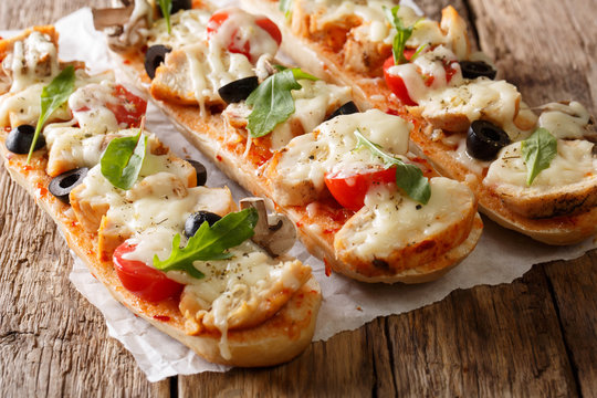 Italian sandwiches pizza casserole: cut baguette baked with chicken, cheese, tomatoes, olives and mushrooms close-up. horizontal
