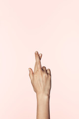 partial view of woman doing crossed fingers gesture isolated on pink background