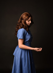 3/4 portrait of brunette lady wearing blue dress, facing away from camera. posed on black studio background.