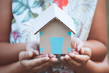 Child and parent holding paper house in hands together as real estate and family home concept