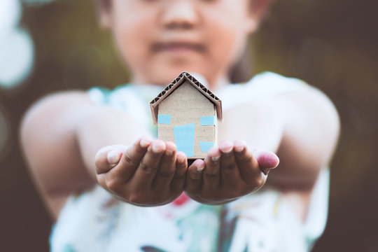 Child holding paper house in hands as real estate and family home concept