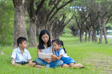 Asian family, mother, son and daughter doing reading activities at the park.
