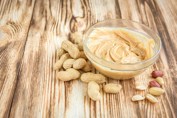 Peanut butter and peanuts on wooden background.