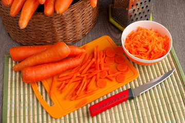 Carrots are whole, grated and sliced. A lot of carrots in a wicker basket. Sliced and grated carrots for cooking. Orange vegetables on an orange cutting board.