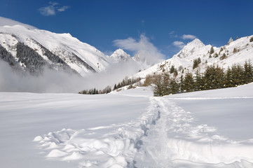 Fototapeta na wymiar Track in the snow crossing a valley in the alpine mountain