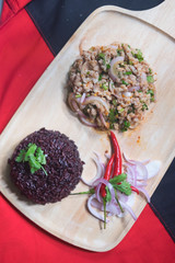 Spicy minced pork salad served with rice berry on wood plate (Larb Moo)