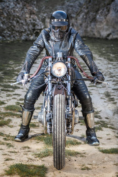 Biker with black leather suit and mask stay on a custom special rat motorbike. Post apocalyptic concept