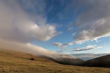 Fototapeta na wymiar Mountain peak with low fog and moving clouds on a blue sky