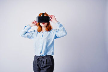 Red haired girl in blue blouse with vr glasses at studio isolated on white.