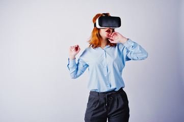 Red haired girl in blue blouse with vr glasses at studio isolated on white.