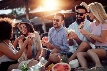Group of friends eating watermelon on the beach