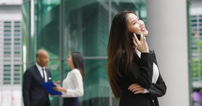 An asian business woman, she is happy and smiling while sending messages, working emails or calling using the phone, outside the office. Concept of: technology, network, oriental