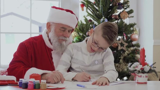The boy sitting on the lap of Santa and draws with a pan