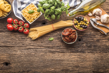 Italian food ingredients pasta olive oil parmesan cheese basil garlic mushrooms tomatoes olives on wooden table