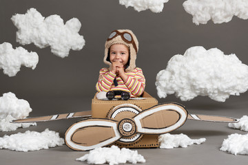 the child girl plays in an airplane made of cardboard box and dreams of becoming a pilot, clouds of...