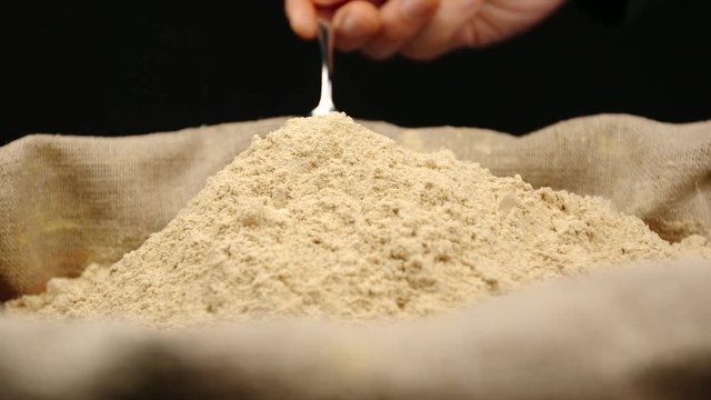 Human hand takes a pinch of a ginger powder by a spoon from a top of pile in a sac