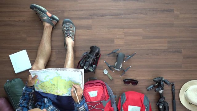 Traveler man and backpack planning vacation travel idea concept trip with map. Top view on wood floor  