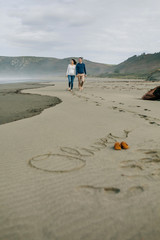 Parents taking a walk with baby name Oliver written in the sand next to his shoes. Selective focus...