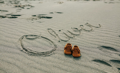 Fototapeta na wymiar Baby name Oliver written in the sand next to his shoes