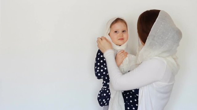 A young Muslim woman in a hijab holds a child in her arms.