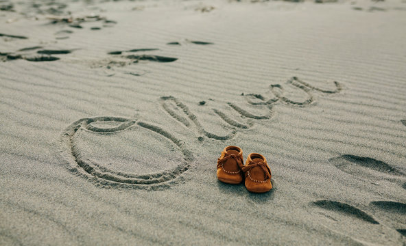 Baby name Oliver written in the sand next to his shoes
