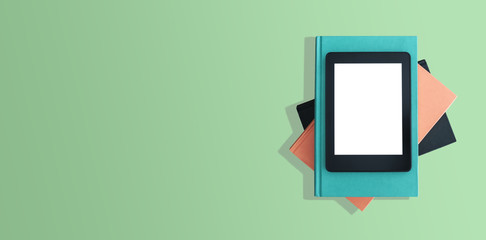 directly above shot of e-book reader, e-reader on stack of books on green desktop