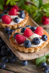  Dessert tarts with raspberries and blueberries on a wooden table.