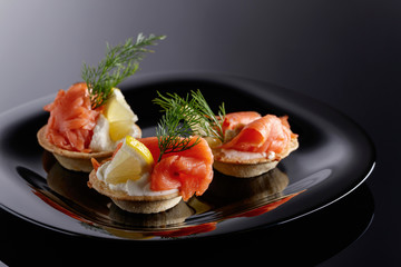 Tartlets with salmon , cream and a slice of lemon on a black plate.