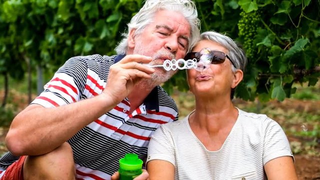 nice beautiful adult couple married in love afer an entire life together have fun playing with bubble soap in the country side outdoor leisure activity. retired happy people play like children