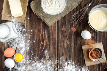 Baking ingredients for cooking chocolate cupcakes or cake. Bowl with sugar, eggs, flour, butter on dark wooden background with copy space.