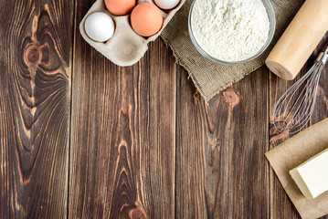 Fototapeta na wymiar Baking ingredients for cooking chocolate cupcakes or cake. Bowl with sugar, eggs, flour, butter on dark wooden background with copy space.