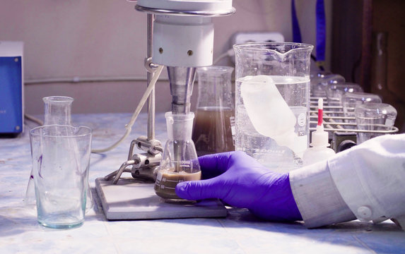 Scientist's hand holding a flask during mixing the sample. Geological laboratory.