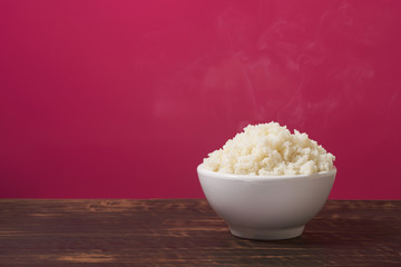 Plain rice in a white bowl with smoke on the table and pink background