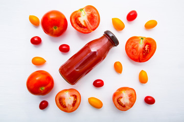 Fresh tomatoes juice in bottle and fresh tomatoes slices on white wooden background.