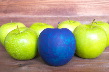 Standing out of the crowd concept, green apples and one painted blue on the wooden background.