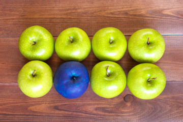 Standing out of the crowd concept, green apples and one painted blue on the wooden background.