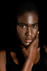 portrait of beautiful african american woman holding hand on chin and looking at camera isolated on black