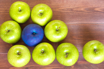 Standing out of the crowd concept, green apples and one painted blue on the wooden background.