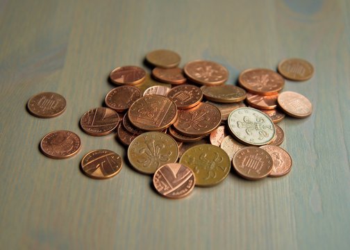A pile of used one and two penny sterling coins on a wooden surface.