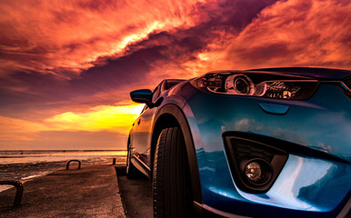 Obraz na płótnie Canvas Blue compact SUV car with sport, modern, and luxury design parked on concrete road by the sea at sunset. Front view of beautiful hybrid car. Driving with confidence. Travel on vacation at the beach.