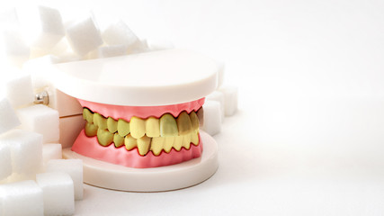 Oral health, tooth decay and cavities and sugary foods destroy the dental enamel concept with plastic medical model of cavity ridden teeth or dentures surrounded by white sugar cubes with copy space