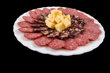 cutting two varieties of sausage and cheese on a white plate and a dark background