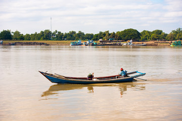 Fototapeta na wymiar MANDALAY, MYANMAR - DECEMBER 1, 2016: A man and a woman in a boat on the Irravarddy river, Burma. Copy space for text.