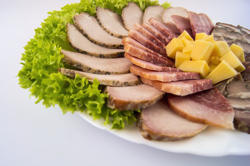 Sausage, meat, roll and cheese, decorated with lettuce leaves on a white plate