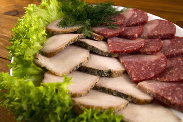 Baked meat and sausage, decorated with lettuce leaves in a white plate on a wooden background