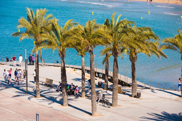 SALOU, TARRAGONA, SPAIN - APRIL 24, 2017: Tourists under the palm trees on the seafront of the Costa Dorada.